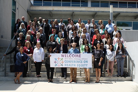 group of people, with one in front holding a banner with text "welcome 2018 wilco wellness alliance conference on health equity"